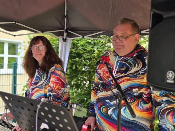 Ein Mann und eine Frau spielen auf einem Sommerfest Musik. Der Mann singt in ein Mikrofon, während die Frau ein Keyboard spielt.