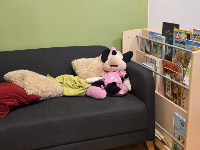 Eine Stoffpuppe von Minnie Maus liegt auf einem Sofa neben einem Bücherregal mit Kinderbüchern. Im Hintergrund ist eine hellgrüne Wand zu sehen.