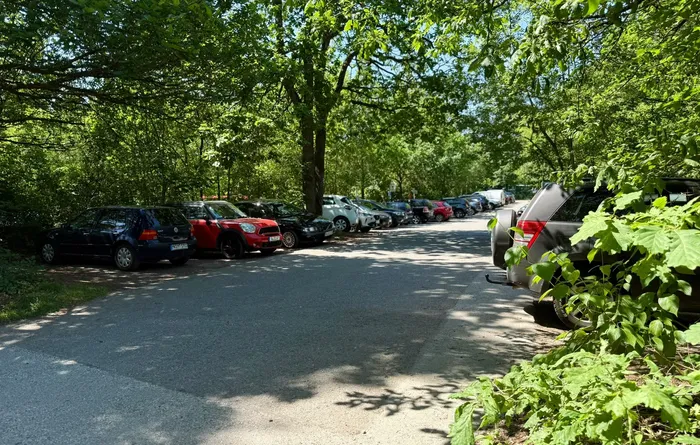 Eine Reihe geparkter Autos säumt eine schattige Zufahrtsstraße, gesäumt von Bäumen und dichter Vegetation. Die Sperrung der Straße zur Glörtalsperre ist erkennbar.