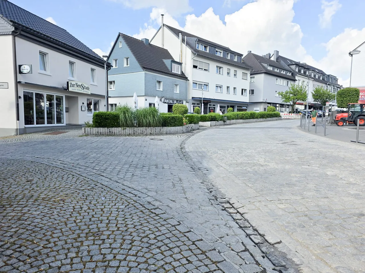Eine gepflasterte Straße mit Geschäften und Häusern entlang der Frankfurter Straße. Im Hintergrund ein roter Traktor.