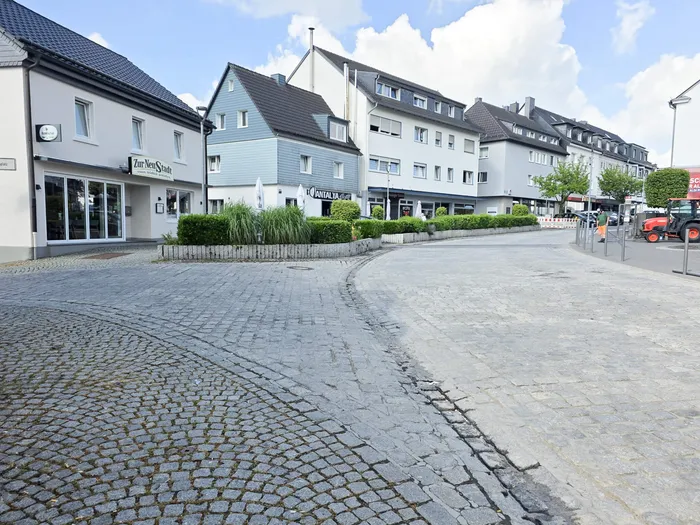 Eine gepflasterte Straße mit Geschäften und Häusern entlang der Frankfurter Straße. Im Hintergrund ein roter Traktor.