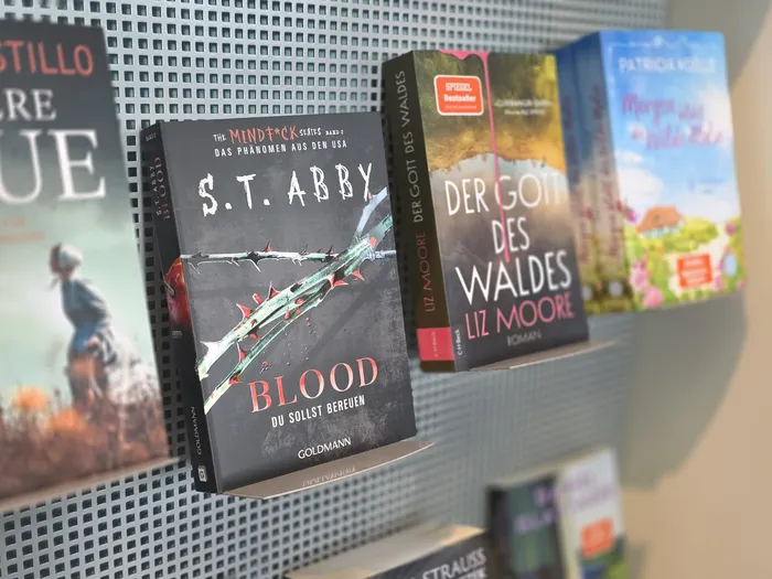 Verschiedene Bücher in einem Wandregal, im Fokus das Buch „Blood“ von S.T. Abby mit einem Stacheldraht-Motiv auf dem Cover.