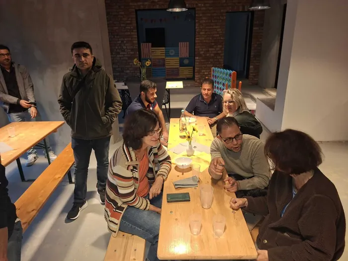 Eine Gruppe von Menschen sitzt und steht an Holztischen bei einem gesellschaftlichen Treffen.