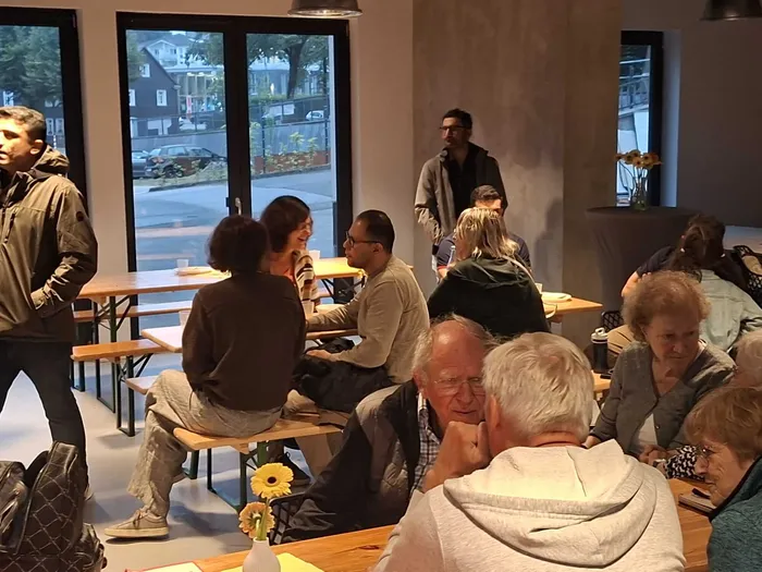 Menschen sitzen an langen Holztischen und unterhalten sich bei einem gesellschaftlichen Treffen im Rahmen des Kultur-Häppchen-Fests.