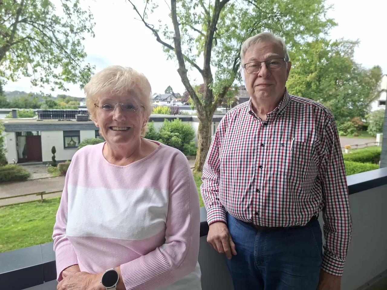 Marianne Struth und Gerd Hegemann stehen lächelnd auf einem Balkon vor Bäumen und Häusern.