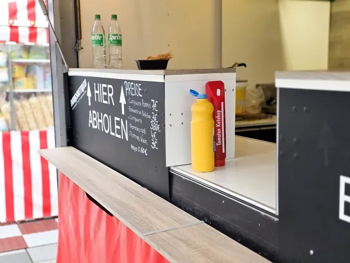 Imbissstand mit Preisschild für Currywurst und Pommes, daneben Flaschen mit Ketchup und Mayonnaise.