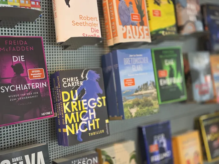 Verschiedene Bücher, darunter Thriller von Freida McFadden und Chris Carter, sind in einem Regal an einer Lochwand ausgestellt.