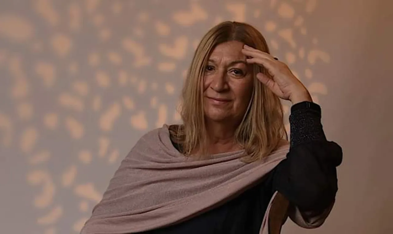 Heike Wulf, eine Frau mit langen, blonden Haaren, blickt nachdenklich in die Kamera und hält ihre Hand an ihre Stirn.