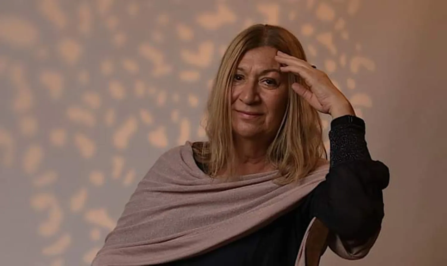 Heike Wulf, eine Frau mit langen, blonden Haaren, blickt nachdenklich in die Kamera und hält ihre Hand an ihre Stirn.