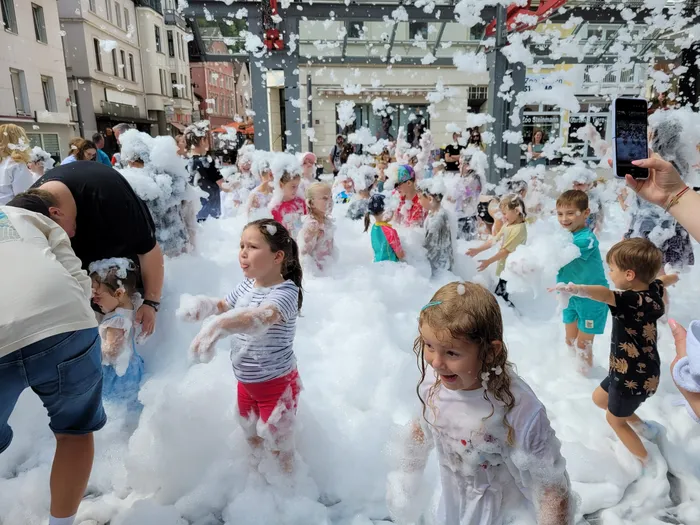 Kinder spielen und lachen inmitten von großen Mengen weißem Schaum bei einer Schaumparty auf einem Marktplatz.