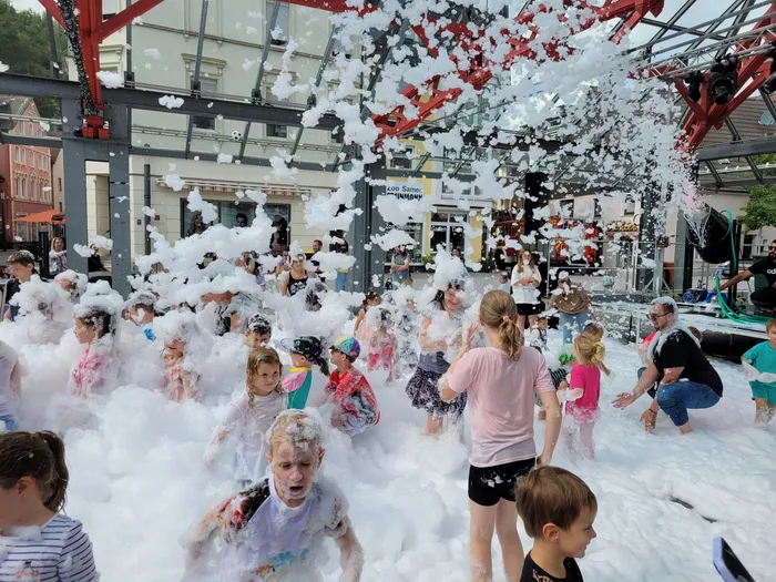 Kinder spielen in einer großen Menge weißem Schaum bei einer Schaumparty unter einer roten Metallkonstruktion.