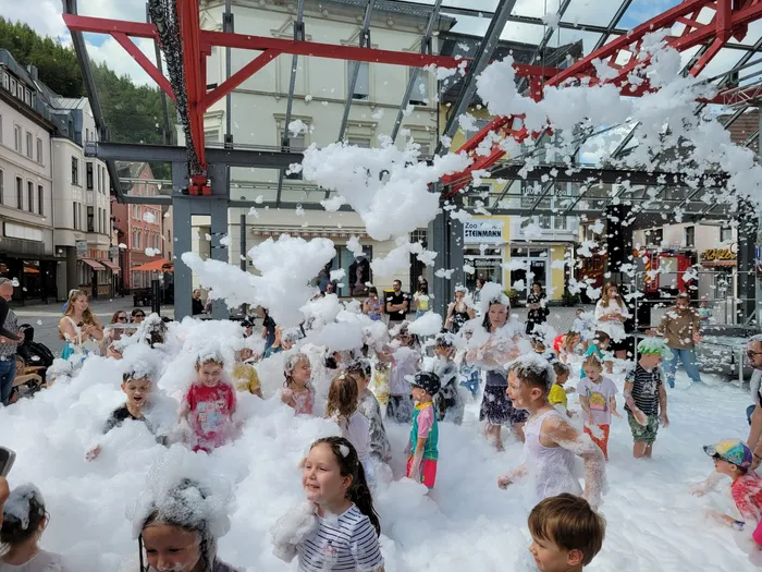 Kinder spielen in einer großen Menge weißem Schaum während einer Schaumparty unter einer roten Metallkonstruktion auf dem Alten Markt.