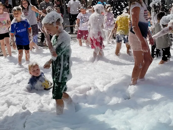 Kinder spielen inmitten von dichtem weißem Schaum bei einer Schaumparty im Freien.