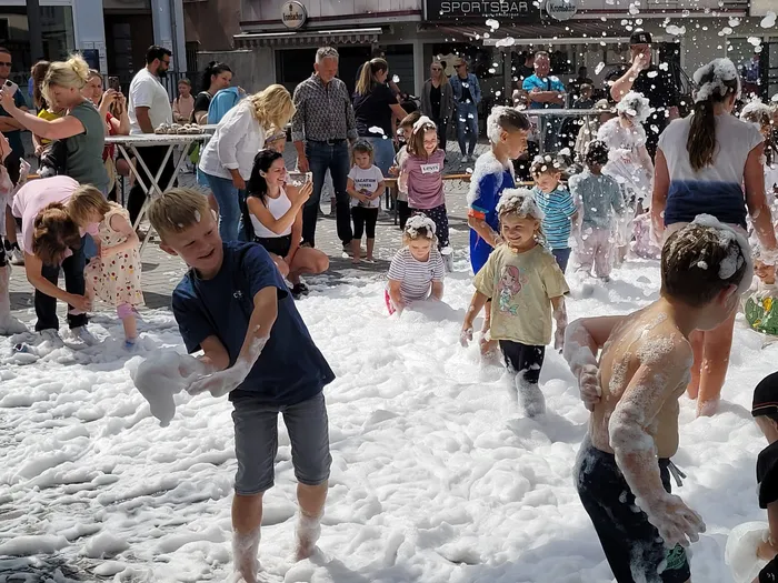 Kinder spielen in einer dicken Schicht aus weißem Schaum bei einer Schaumparty auf dem Alten Markt.