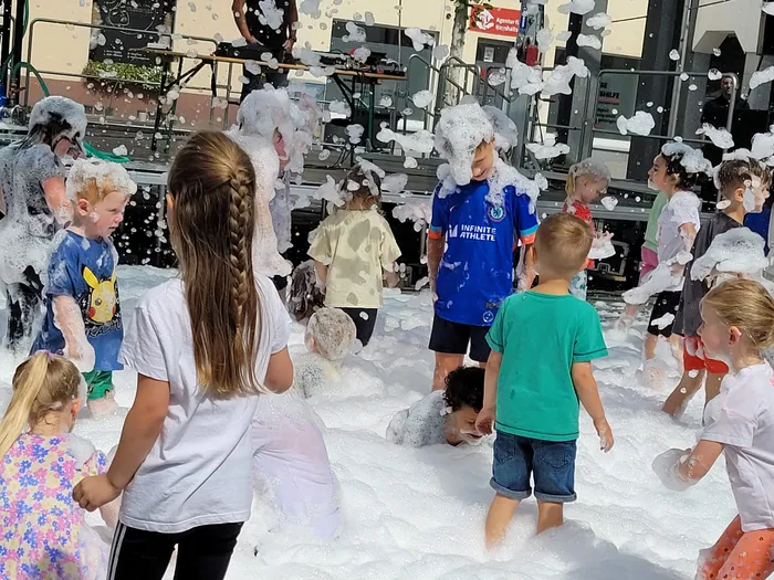 Mehrere Kinder spielen in einer großen Menge weißem Schaum, der teilweise ihre Köpfe bedeckt.
