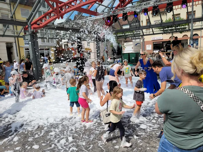 Kinder spielen auf einer Schaumparty auf dem Alten Markt inmitten von weißem Schaum unter einer Bühnenkonstruktion.
