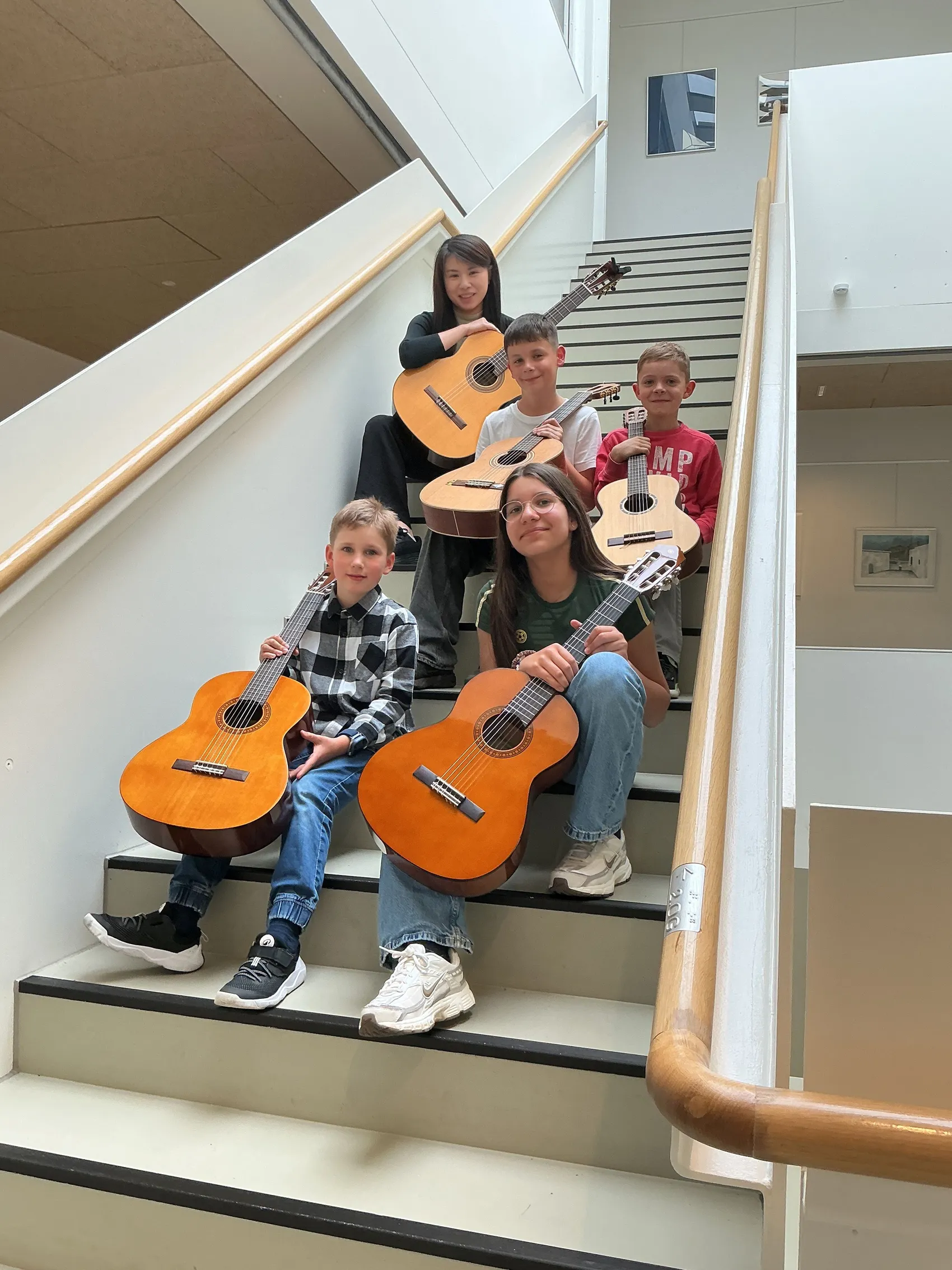 Fünf junge Musiker und Musikerinnen sitzen auf einer Treppe und halten Gitarren. Sie lächeln in die Kamera.