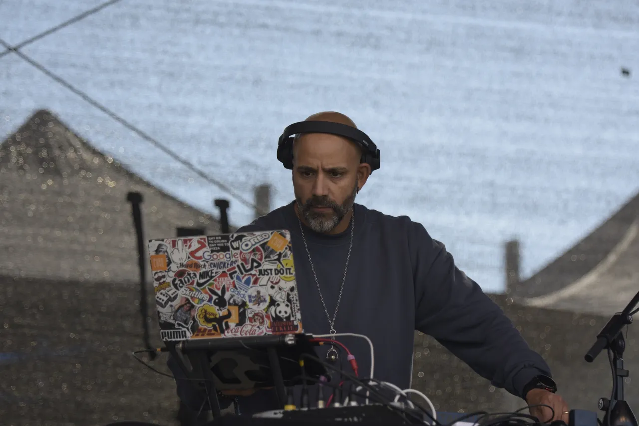 DJ Shorty mit Kopfhörern bedient einen mit Stickern beklebten Laptop auf der Collabo Stage.
