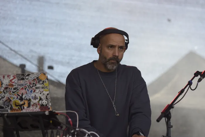 Shorty mit Kopfhörern und Bart blickt an einem mit Stickern beklebten Laptop vorbei.