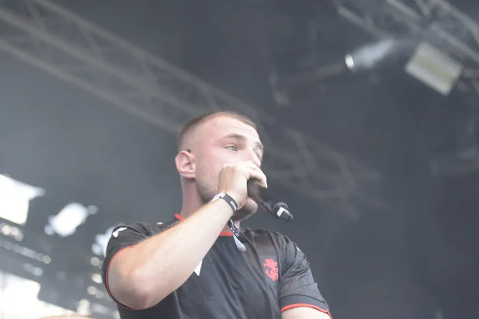 Ein Mann singt bei einem Auftritt auf der Collabo Stage in ein Mikrofon vor einer nebligen Bühnenkulisse.