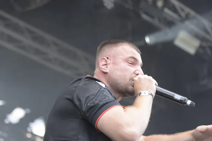Ein Mann mit kurzen Haaren und Bart singt in ein Mikrofon während eines Auftritts auf einer Bühne.