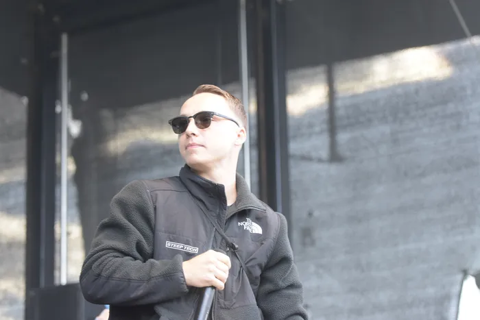 Ein Mann mit Sonnenbrille und einer schwarzen The North Face Jacke hält ein Mikrofon.