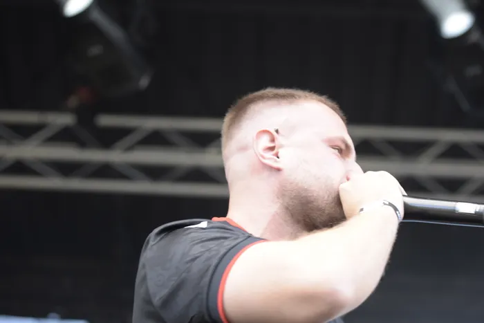 Ein bärtiger Mann singt im Profil in ein Mikrofon auf einer Bühne.