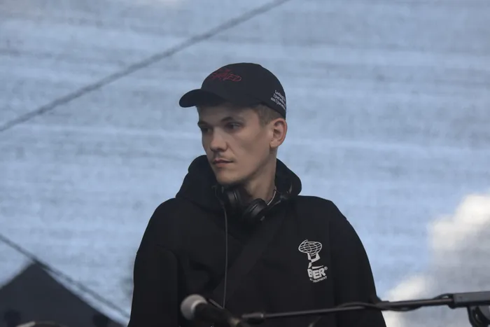 Ein junger Mann mit schwarzer Cap und schwarzem Hoodie trägt Kopfhörer um den Hals und blickt zur Seite.