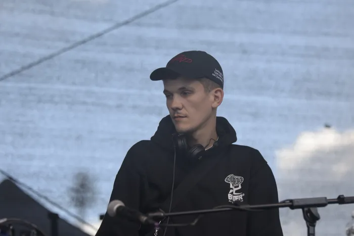 Ein junger Mann mit schwarzer Cap und schwarzem Hoodie trägt Kopfhörer um den Hals und blickt zur Seite.
