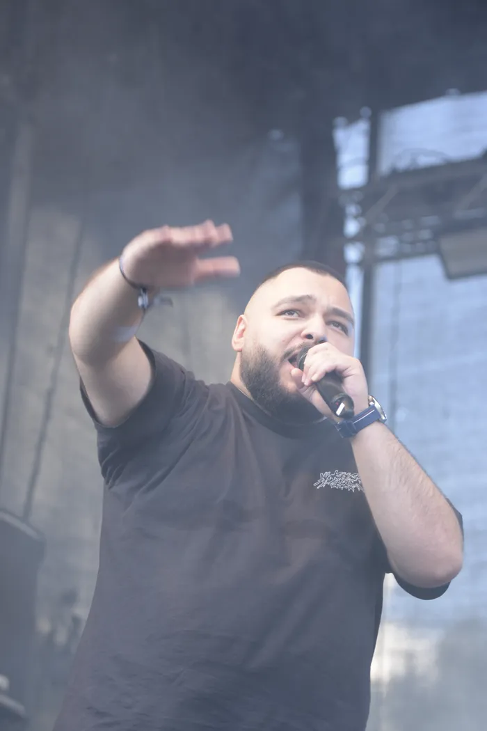 Ein bärtiger Mann im schwarzen T-Shirt singt in ein Mikrofon auf einer vernebelten Bühne.