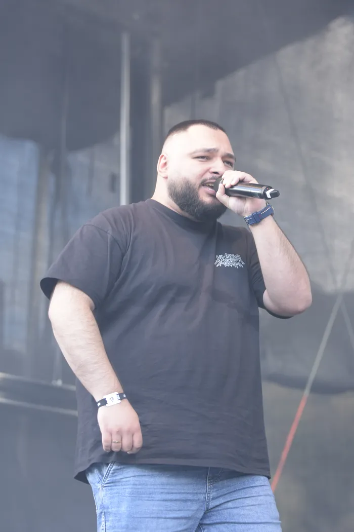 Ein bärtiger Mann im schwarzen T-Shirt singt in ein Mikrofon auf einer vernebelten Bühne.