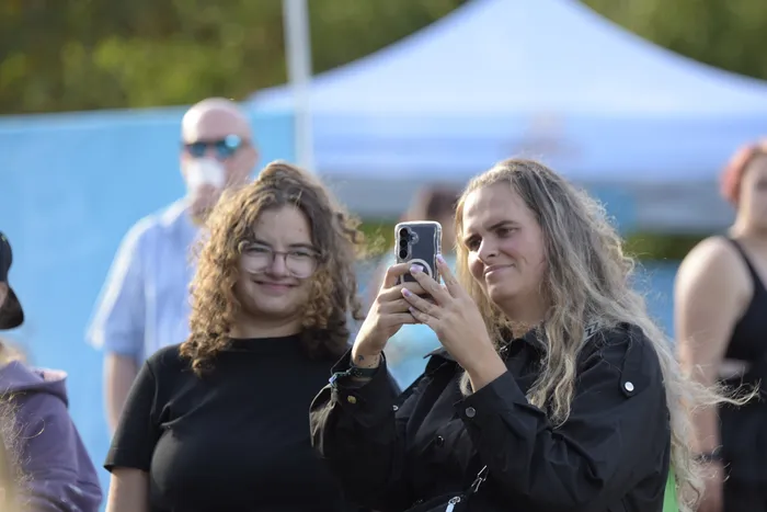 Eine junge Frau fotografiert mit ihrem Smartphone, während eine weitere junge Frau mit lockigem Haar und Brille neben ihr steht.