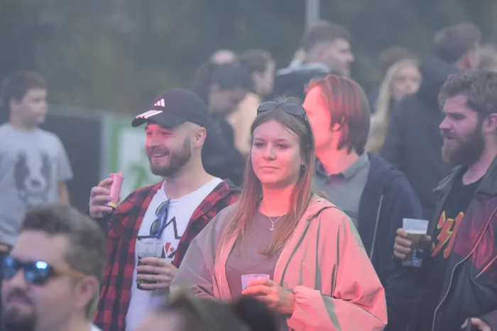 Eine Menschenmenge in nebliger Atmosphäre bei einem Musikfestival, einige Personen halten Getränke.
