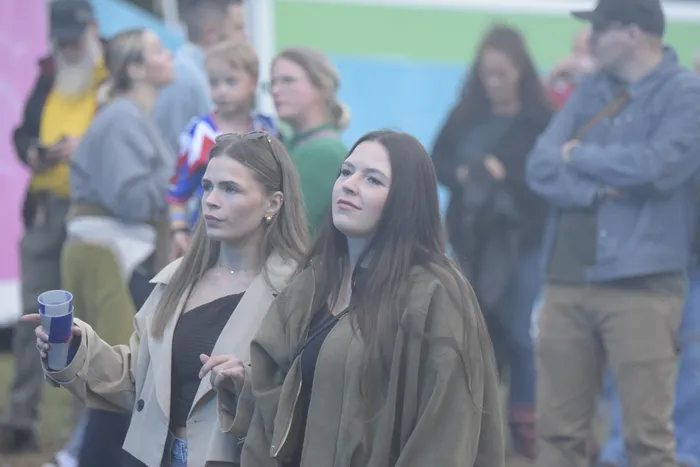Zwei junge Frauen blicken in einer Menschenmenge aufmerksam in Richtung einer Bühne.