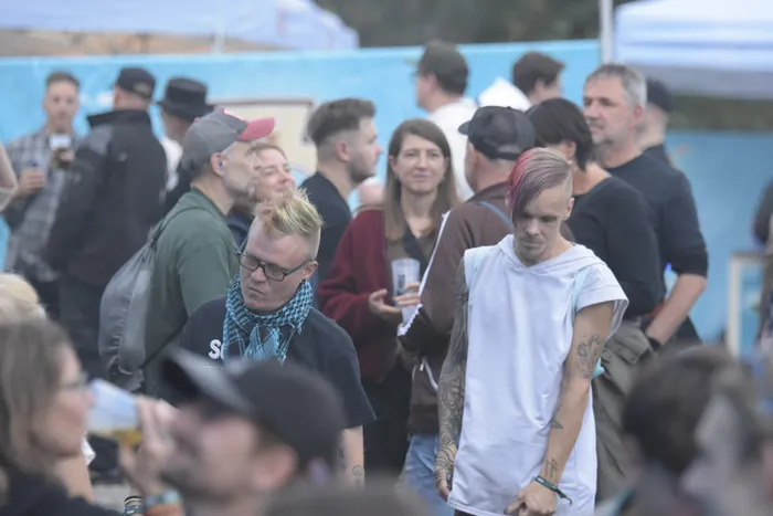 Ein Mann mit rötlich-pinken Haaren und weißem T-Shirt steht in einer Menschenmenge bei einem Open-Air-Event.