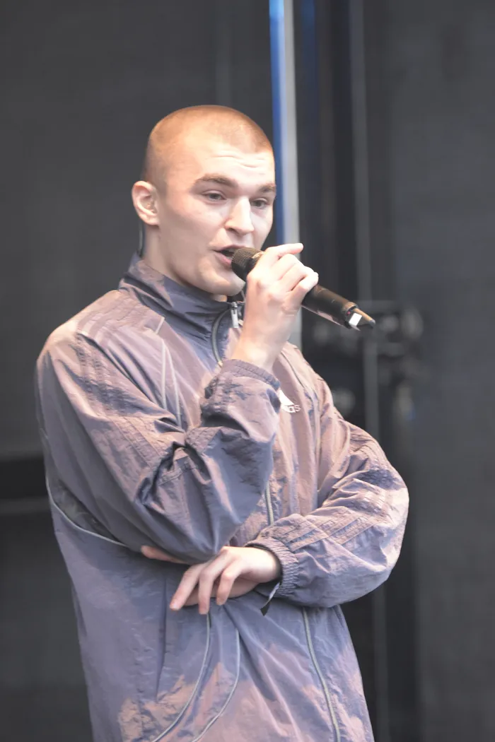 Hexer singt in ein Mikrofon auf der Collabo Stage und trägt eine gemusterte graue Trainingsjacke.