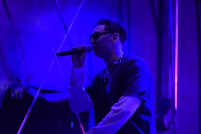 Sampagne singt mit einem Mikrofon unter blauem und violettem Bühnenlicht.