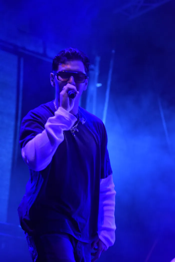 Sampagne singt mit Sonnenbrille unter blauem Bühnenlicht in ein Mikrofon.