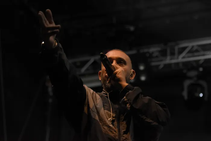 Der Rapper Azad performt auf einer Bühne, hält ein Mikrofon an den Mund und streckt einen Arm mit einer Geste nach oben.