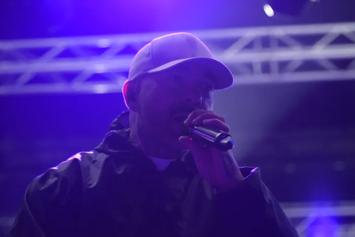 Der Rapper Azad performt unter violettem Bühnenlicht mit einem Mikrofon und trägt eine Kappe.