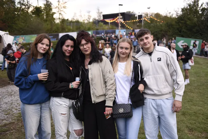 Fünf junge Menschen posieren für ein Foto auf einer Wiese vor einer Menschenmenge bei einem Open-Air-Event.