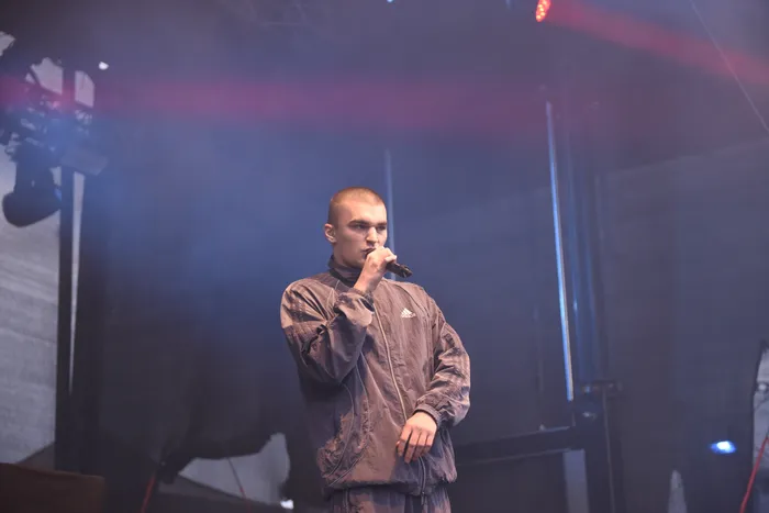 Hexer performt mit einem Mikrofon auf der Collabo Stage in einem grauen Trainingsanzug unter blauem und rotem Bühnenlicht.