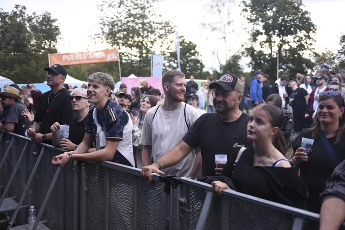 Menschenmenge lehnt an einer Metallabsperrung bei einem Open-Air-Event vor einem „PUEBLO AREA“-Banner.