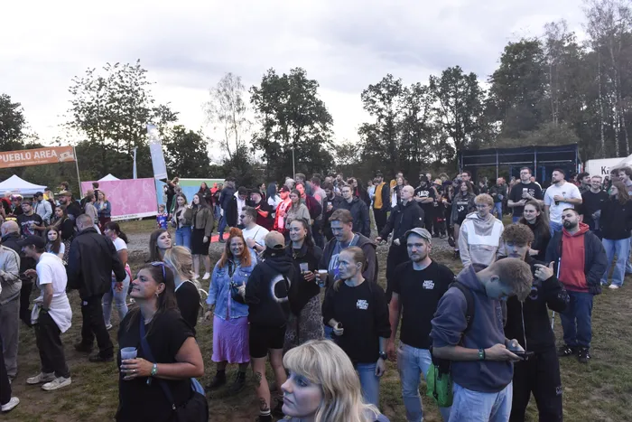 Eine große Menschenmenge bei einem Open-Air-Event vor Zelten und Bäumen unter bewölktem Himmel.