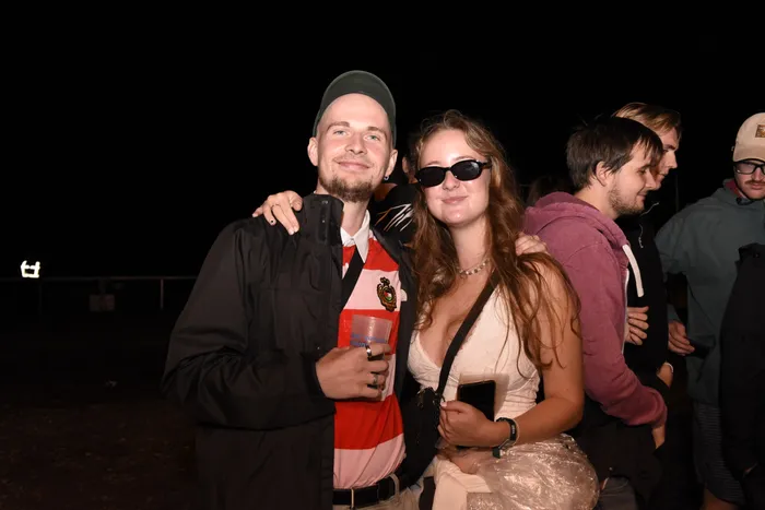Ein Mann in einem rot-weiß gestreiften Shirt hält einen blauen Becher, während eine Frau mit Sonnenbrille neben ihm posiert.