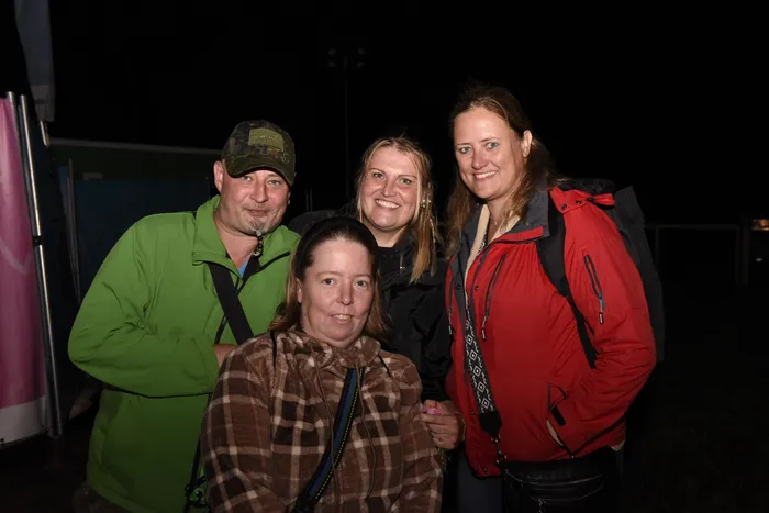 Vier lächelnde Besucher in Jacken posieren nachts für ein gemeinsames Gruppenfoto.