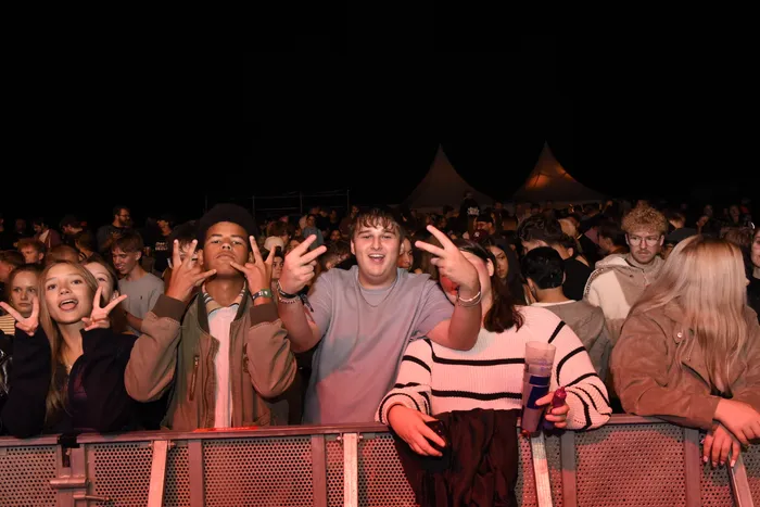 Eine Gruppe junger Menschen macht Handzeichen hinter einer Metallabsperrung bei einem Musikfestival.