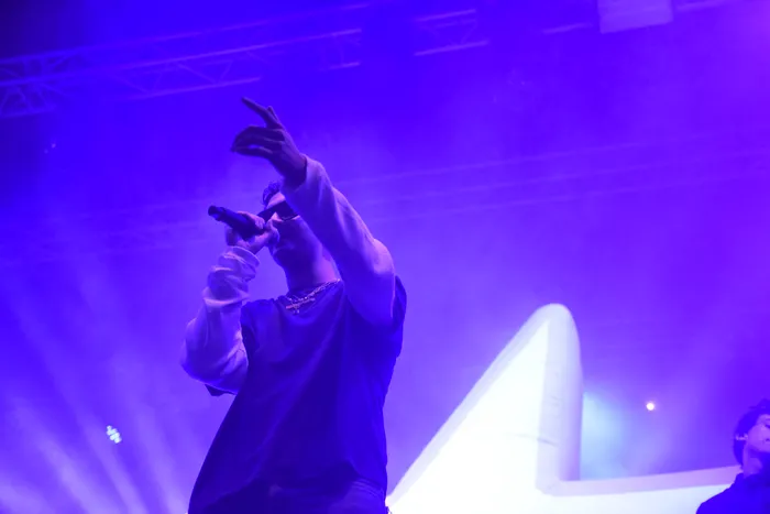 Sampagne singt mit erhobener Hand in ein Mikrofon auf einer Bühne unter blauem Licht.