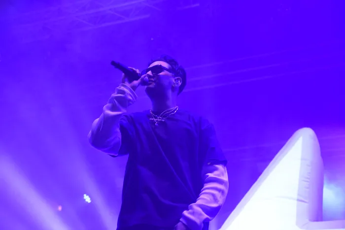 Sampagne singt mit Sonnenbrille unter violettem Bühnenlicht in ein Mikrofon.