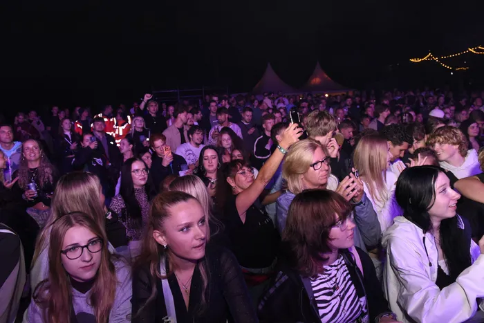 Eine Menschenmenge bei einem nächtlichen Event blickt in Richtung einer Bühne, einige Personen halten ihre Smartphones hoch.